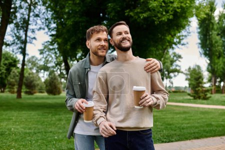 A bearded gay couple in casual attire walk through a park, enjoying a sunny afternoon and coffee together.