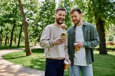 Two bearded gay men share a laugh while enjoying coffee in a lush green park.