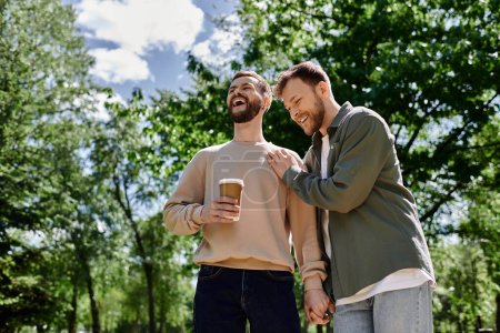 A bearded gay couple shares a laugh while walking through a park on a sunny day.