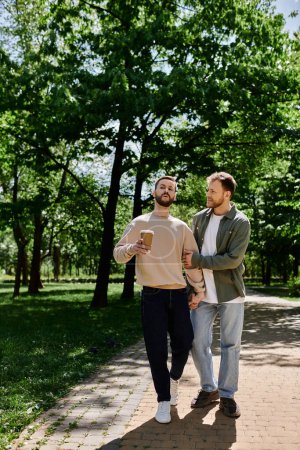 Zwei bärtige schwule Männer in lässiger Kleidung halten sich an den Händen und gehen einen Pfad in einem üppig grünen Park entlang.