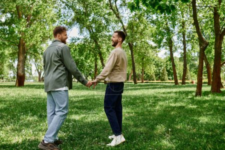 A bearded gay couple walks hand-in-hand through a lush green park, smiling and enjoying each others company.