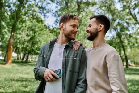 Dos hombres barbudos con ropa casual se paran juntos en un parque verde, compartiendo un momento de amor.