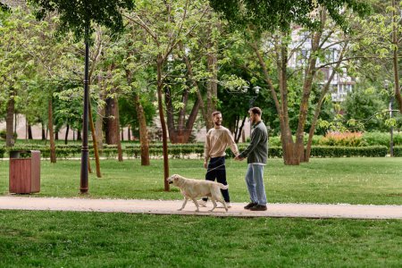 Ein bärtiges schwules Paar geht mit seinem Labrador Retriever auf einem Weg in einem Park spazieren. Das Paar ist lässig gekleidet und lächelt, genießt die gemeinsame Zeit.