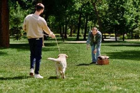 Zwei bärtige Männer spielen mit ihrem Labrador Retriever in einem sonnigen Park.