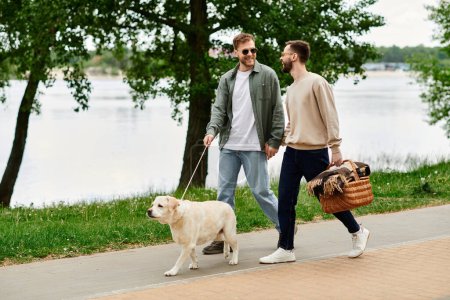Ein schwules Paar spaziert mit seinem Labrador Retriever durch einen grünen Park zu einem Picknickplatz am See.