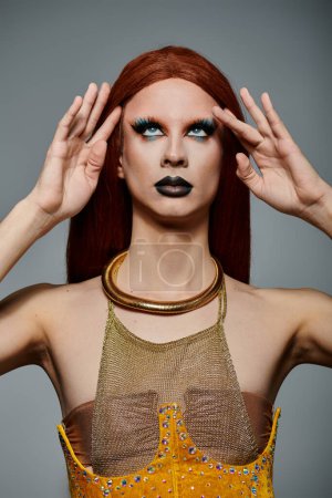 A drag queen poses with her hands on her head, looking up in a dramatic pose.