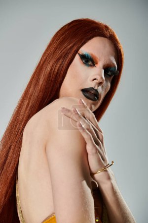 Foto de A drag diva with long red hair poses for a portrait in bold makeup. - Imagen libre de derechos