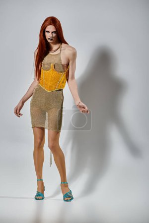 Una drag queen glamorosa posa en un vestido de oro brillante y tacones a juego.