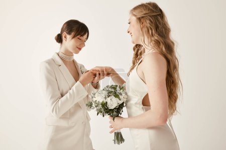 Deux jeunes femmes en tenue blanche échangent des bagues lors de leur cérémonie de mariage.