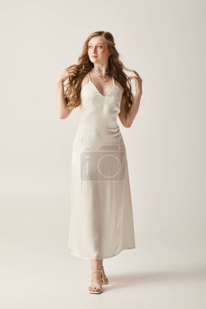 Eine schöne junge Braut posiert in einem fließenden weißen Brautkleid vor weißem Hintergrund.