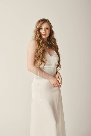 Una hermosa novia joven con un vestido de novia blanco está de pie sobre un fondo blanco. Su cabello largo y fluido aumenta su elegancia.
