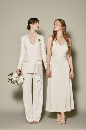 Dos mujeres jóvenes, vestidas de blanco, se toman de la mano durante la ceremonia de su boda. La foto celebra el amor LGBTQ + y las interpretaciones modernas del atuendo tradicional de la boda.