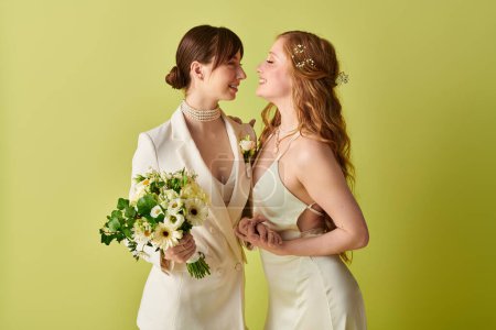 Ein junges lesbisches Paar in weißer Hochzeitskleidung umarmt sich auf grünem Hintergrund und symbolisiert damit ihre Liebe und ihr Engagement.