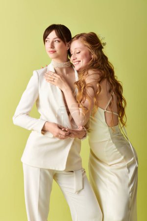 Zwei junge Frauen in weißer Hochzeitskleidung umarmen sich vor grünem Hintergrund.