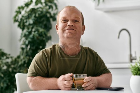 A man with inclusivity sits at a table, holding a cup of tea, in his cozy home.