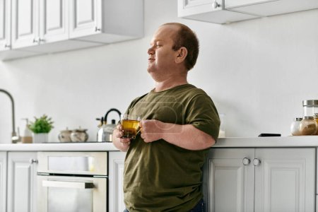 Un hombre con inclusividad se para en su cocina, vestido casualmente, disfrutando de una taza de té.