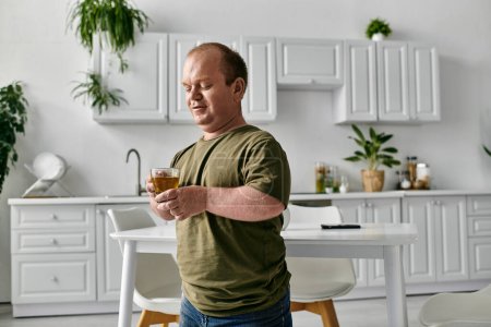 Un homme avec inclusivité se tient dans sa cuisine, vêtu avec désinvolture, tenant une tasse de thé.