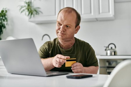 Ein Mann mit Inklusivität sitzt an einem Küchentisch und kauft online mit Kreditkarte ein.