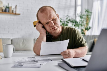 Un homme inclusif s'assied à une table, examinant les factures et une carte de crédit, apparemment préoccupé par ses finances.