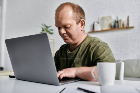 A man with inclusivity works on his laptop in his home office, dressed casually and comfortably.