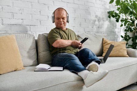 Un hombre con inclusividad usando auriculares se sienta en un sofá en casa, disfrutando de un momento de paz.