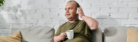 Ein Mann mit Kopfhörern und lässiger Kleidung entspannt sich zu Hause auf einer Couch und hält eine Tasse Kaffee in der Hand.