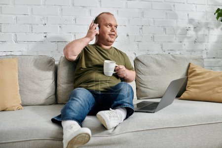 A man with inclusivity sits comfortably on a couch, wearing headphones and enjoying a cup of coffee.