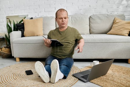 Un hombre con inclusividad se sienta en el suelo frente a un sofá, trabajando en un cuaderno con una computadora portátil cerca.