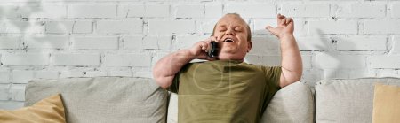 A man with inclusivity in casual attire smiles while on a phone call at home.
