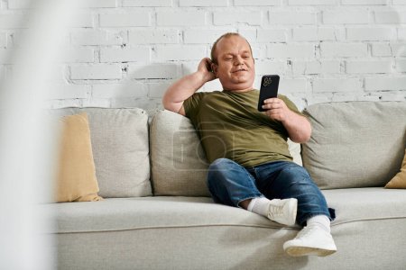 A man with inclusivity relaxes on a sofa in his home, scrolling through his phone.