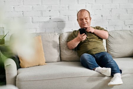 Un homme inclusif est assis sur un canapé dans son salon, vérifiant son téléphone avec désinvolture.