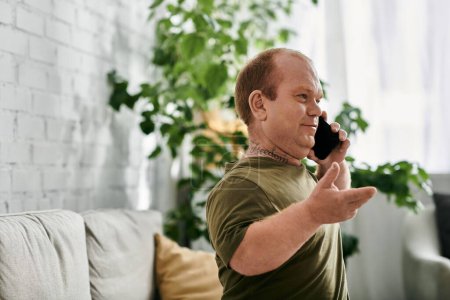 A man with inclusivity in casual attire talks on the phone while sitting in his home.