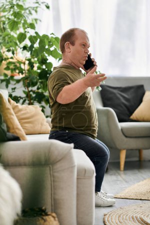 A man with inclusivity sits on a couch in a living room, talking on the phone.