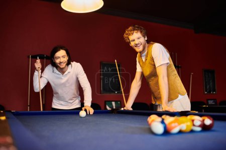 Two men in casual clothing play pool together in a dimly lit room.
