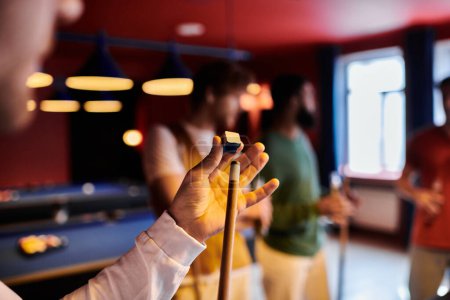 A man holds a cue stick and chalk while playing billiards with friends.