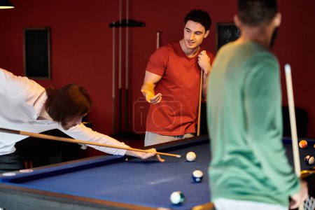 Friends play billiards in a dimly lit room, focusing on the shot.