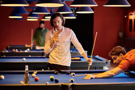 Freunde spielen Pool in einer schwach beleuchteten Bar, einer hält ein Bier in der Hand, während der andere einen Schuss abgibt.