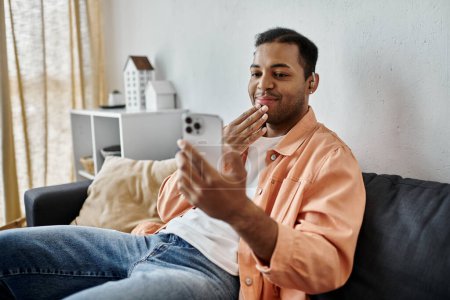 Ein afroamerikanischer Mann sitzt auf einer Couch in seinem Haus und unterhält sich bei einem Videoanruf lächelnd, während er bei der Person am anderen Ende unterschreibt..