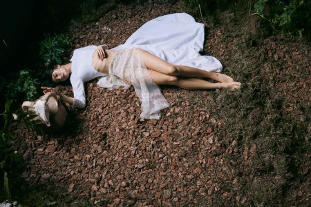 A woman lies on the ground, wearing a white dress.