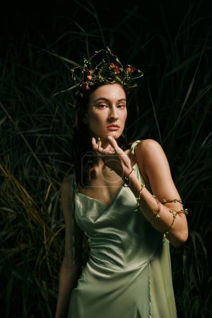 Woman in green dress gracefully poses in forest with floral crown.
