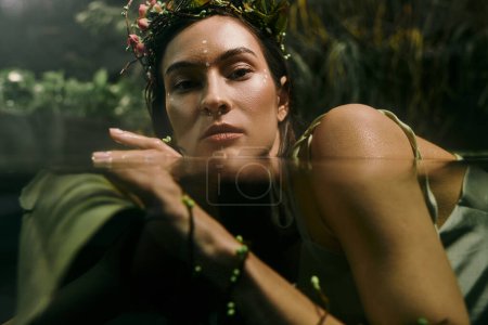 A woman wearing a floral crown poses in a swamp, her head partially submerged in water.