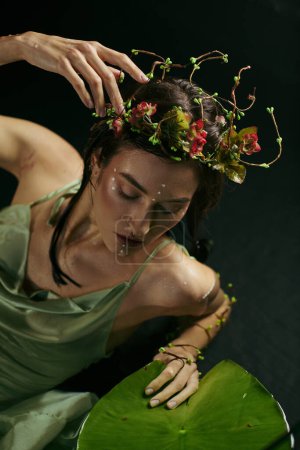 A young woman with a floral crown and green attire poses gracefully near a swamp.