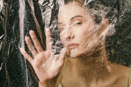 Una cara de mujer está parcialmente oscurecida por una lámina de plástico, gotas de lluvia aferradas a su superficie.