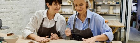 Photo for Two mature women wearing aprons work on a pottery project in a studio. - Royalty Free Image