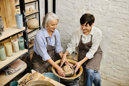 Two mature women working together on a pottery wheel in a cozy studio.