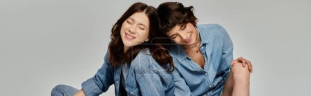 A young lesbian couple, both wearing denim, poses for a photo shoot against a gray backdrop.