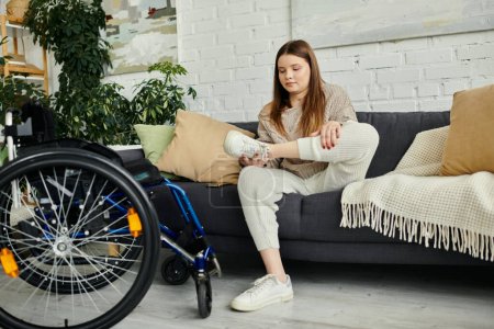 Eine junge Frau im Rollstuhl zieht ihre Turnschuhe an, während sie auf einer Couch in ihrem Wohnzimmer sitzt.