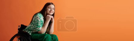 Téléchargez les photos : Une jeune femme handicapée dans une robe verte vibrante assise en toute confiance dans un fauteuil roulant sur un fond orange. - en image libre de droit
