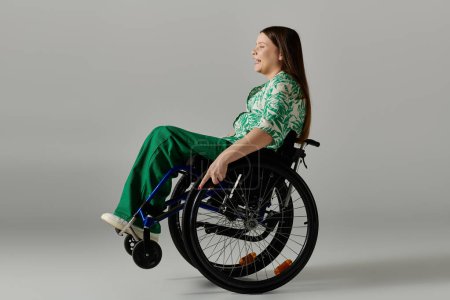 A young woman in green attire sits in a wheelchair against a grey background, smiling brightly.