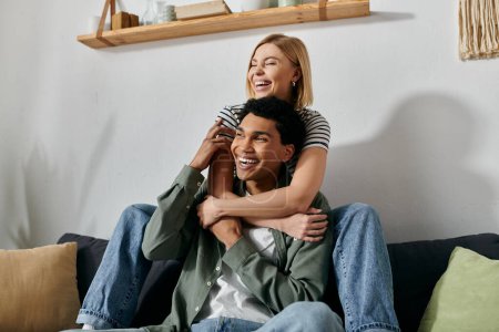 A young interracial couple shares a joyful moment on a couch in their modern apartment.